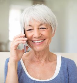 Eine ältere Frau mit kurzen grauen Haaren lächelt zufrieden, während sie ein Telefongespräch führt. Sie sitzt in einem hellen Raum, der eine entspannte und freundliche Atmosphäre vermittelt. Das Bild symbolisiert die einfache und persönliche Kontaktaufnahme mit Alltagshilfe365, um Unterstützung im Alltag oder im Haushalt zu erhalten.